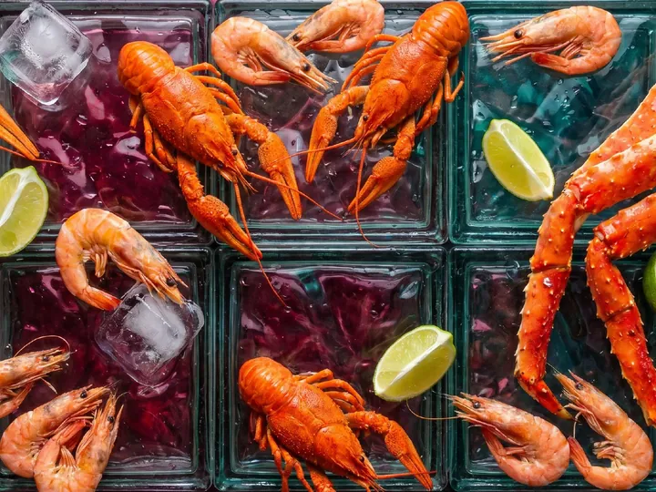Варёные раки, ноги камчатского краба и креветки на стеклоблоках со льдом и лаймом